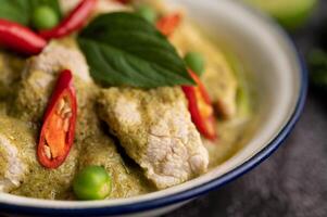 Pork green curry in a white bowl with spices on a black cement photo