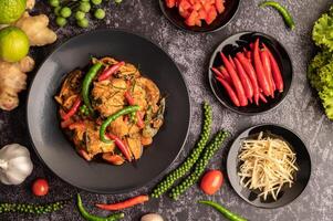 Stir-fried spicy Catfish in black plate with spices on black cement. photo