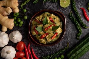 Pork green curry in a brown bowl with spices on a black cement photo