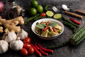 Pork green curry in a white bowl with spices on a black cement photo