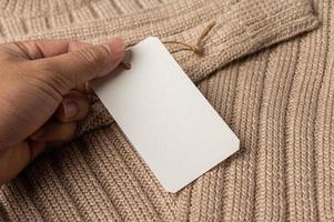 una mano sosteniendo una etiqueta blanca en un suéter marrón. foto