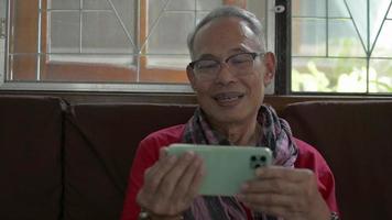 Elderly grandfather in eyeglasses having video call on smartphone.