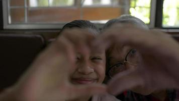 Happy grandfather and granddaughter make heart shape hand gesture.