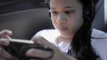 Girl wears headphones playing online games while sitting in the car.
