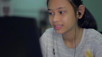 Jovencita lleva auriculares hablando con amigos a través de videollamadas en el portátil video