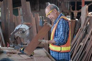 Senior Asian carpenter cutting timber in factory. photo