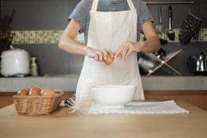 Female cook in a white apron is cracking an egg in home's kitchen. photo