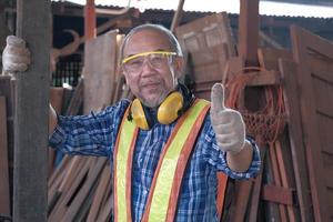Senior male carpenter working and thumb up in wooden sawmill factory. photo