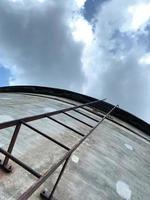 View looking up a rusted steel ladder going up a concrete water tank photo