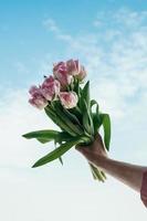 bouquet of pink flowers in hand against blue sky background photo