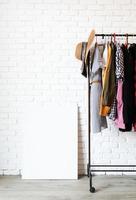 Rack with colorful clothes on hangers and frame canvas for mock up photo