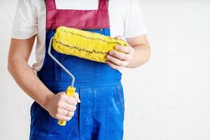 closeup of a worker in blue overalls with a roller for coloring walls photo