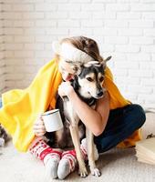 Funny young woman in yellow plaid sitting on the floor hugging her dog photo