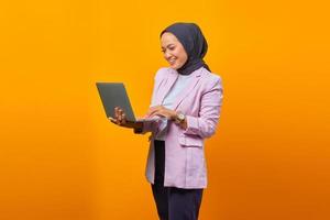 Retrato de mujer asiática sonriente sosteniendo portátil sobre fondo amarillo foto