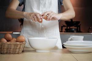 cocinera con un delantal blanco está rompiendo un huevo en la cocina de casa.