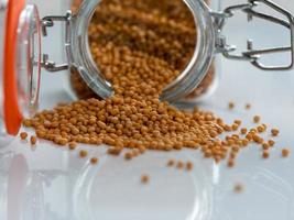 Dry mustard seeds in a glass bottle, white background. Close-up macro photo