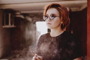 chica con pelo rojo corto y gafas de sol de espejo fumando cigarrillo foto