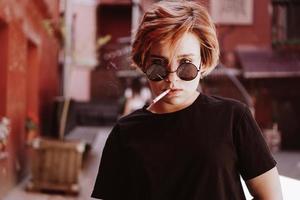 chica con pelo rojo corto y gafas de sol de espejo fumando cigarrillo foto