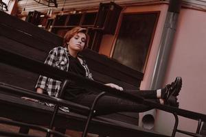 Young woman with short red hair in a bar put her legs on table photo