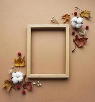 Autumn composition. Photo frame, flowers, leaves on brown background