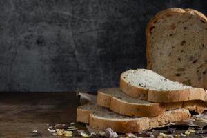 Pan de trigo integral de grano en rodajas sobre fondo de madera rústica oscura foto