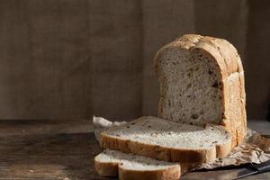Pan de trigo integral de grano en rodajas sobre fondo de madera rústica oscura foto