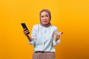 Shocked Asian woman holding smartphone and raised hand photo