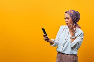 Conmocionada mujer asiática mirando smartphone con la boca abierta foto