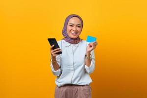 Cheerful Asian woman holding smartphone and showing blank card photo