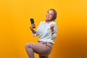 Emocionada mujer asiática sosteniendo teléfono móvil celebrando la suerte foto