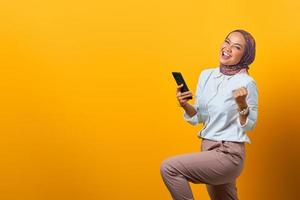 Emocionada mujer asiática sosteniendo teléfono móvil celebrando la suerte foto
