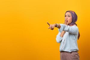 Retrato de mujer asiática sorprendida apuntando al espacio en blanco con el dedo foto