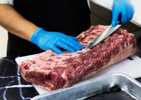 El chef corta la carne cruda con un cuchillo en una tabla, el cocinero corta la carne cruda foto