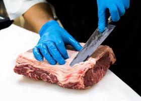 El chef corta la carne cruda con un cuchillo en una tabla, el cocinero corta la carne cruda foto