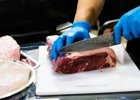 El chef corta la carne cruda con un cuchillo en una tabla, el cocinero corta la carne cruda foto