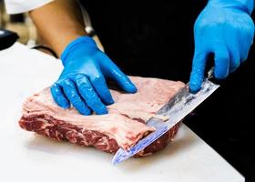 chef cuts raw meat with a knife on a board, Cook cuts raw meat