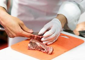 Chef cortando carne cruda fresca con un cuchillo en la cocina foto