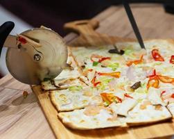 Primer plano de un cortador de pizza en la pizza italiana en la mesa de madera foto