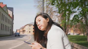 femme asiatique assise à l'arrêt de bus pour attendre un bus avec un smartphone video