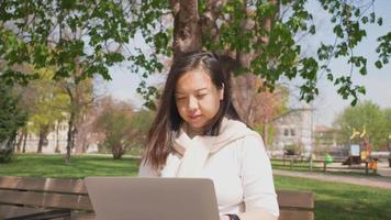 donna asiatica seduta lavoro sul computer portatile al parco. Lavorare all'aperto