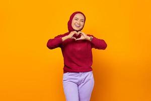 Smiling young girl in red sweater showing heart with two hands, photo
