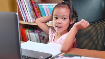 süßes kleines Schulmädchen, das während ihres Online-Studiums Hausaufgabenmathematik studiert.