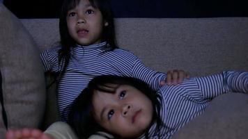 lindos niños pequeños sentados en el sofá y viendo dibujos animados en la televisión. video