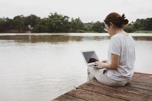 Adult woman using computer to work remotely from riverside photo