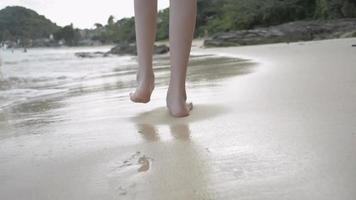 garota caminhando na praia com salpicos de água do mar na areia. video
