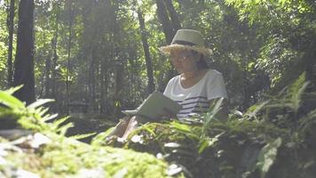 Woman sitting under the tree and writing on a notebook in the forest. video