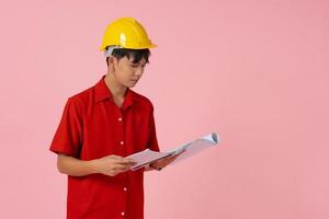 joven ingeniero asiático de pie sobre fondo rosa foto