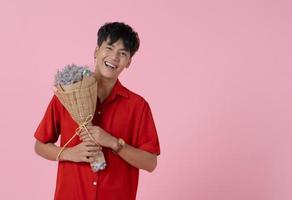 Young asian smiling man holding bouquet of flowers on pink background photo