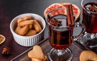 Navidad vino tinto caliente con especias y frutas sobre una mesa oscura. foto