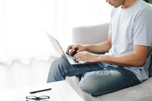 Young man sitting on the sofa typing on the laptop for online working. photo